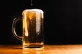 Cold beer with foam in a mug, on a wooden table and a dark background with blank space for a logo or text. Stock Photo mug of cold Royalty Free Stock Photo