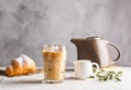 Cold black coffee with ice cubes in tall glass and fresh croissant. Refreshing coffee drink on a table gray background. Royalty Free Stock Photo