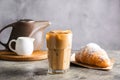 Cold black coffee with ice cubes in tall glass and fresh croissant. Refreshing coffee drink on a table gray background Royalty Free Stock Photo