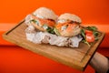 Cold burgers with salmon, sauce, cucumber, tomato and arugula served in the wooden plate Royalty Free Stock Photo