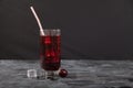 Cold cherry juice with ice in a glass with a straw stands on a black background. Copy spaes