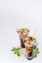 Cold cocktail cuba libre in two wet glasses with straw, pieces lime, mint on soft modern white background, top view, border. Royalty Free Stock Photo