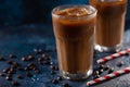 Cold coffee with ice cubes and milk on a background with coffee grains and tubes, dark blue background, summer, cool drinks Royalty Free Stock Photo