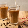 Cold coffee pouring in cream, milk in transparent glasses with ice and straws, on a wooden background, a cooling drink, refreshing Royalty Free Stock Photo