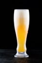 Glass of fresh cold light beer with froth flowing on the table and beautiful spilled beer on a black background