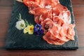 Cold cuts on stone plate with prosciutto, bacon, salami and sausages decorated with flowers on wooden background. Royalty Free Stock Photo