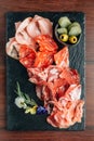 Cold cuts on stone plate with prosciutto, bacon, salami and sausages decorated wth flowers on wooden background. Royalty Free Stock Photo