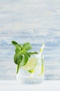 Cold detox summer mineral water with lime, mint, ice, straw on soft blue wood background, copy space.