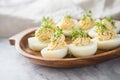 Cold deviled eggs filled with cream cheese, cress and herbs on wooden plate, linen towel and light marble background for eastern,