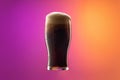 One full glass of frothy dark beer isolated over gradient purple and orange color background in neon. Concept of alcohol