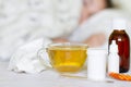 Cold and flu medicines and hot tea with lemon, in the background sick girl is lying in bed Royalty Free Stock Photo