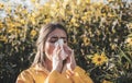 Cold flu season, runny nose. Flowering trees in background. Young girl sneezing and holding paper tissue in one hand and