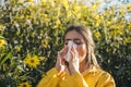 Cold flu season, runny nose. Flowering trees in background. Young girl sneezing and holding paper tissue in one hand and