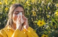 Cold flu season, runny nose. Flowering trees in background. Young girl sneezing and holding paper tissue in one hand and