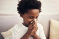 Cold and flu season. Sick african american boy with afro blowing nose into tissue. Child suffering from a runny nose or Royalty Free Stock Photo