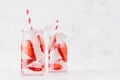 Cold fresh fruit beverage of ripe strawberry with ice, soda water, bubbles, funny striped straw on simple soft bright white. Royalty Free Stock Photo