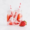 Cold fresh fruit beverage of ripe strawberry with ice, soda water, bubbles, funny striped straw on simple soft bright white wood. Royalty Free Stock Photo