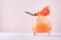 Cold fresh homemade grapefruit cocktail with ice, rosemary and pieces citrus on pastel pink background.