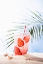 Cold fresh pink alcohol cocktail with ice, straw in plastic mug in sunlight on tropical beach with ocean view, vertical. Takeaway. Royalty Free Stock Photo