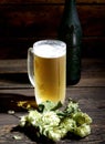 Cold frothy beer in glass, bottle and hops on a wooden background