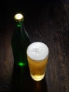 The cold frothy beer in a glass and a green bottle on a dark wooden background Royalty Free Stock Photo