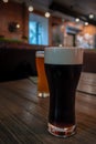 Cold Glass of dark kraft Beer standing on wooden table at a bar. Foam on the Stout beer. Pub in the background. Royalty Free Stock Photo