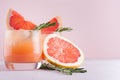 Cold grapefruit cocktail with ice, rosemary and pieces grapefruit on pastel pink background, closeup. Royalty Free Stock Photo
