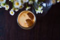 Cold latte, coffee with milk and ice in beautiful glass on dark background with small flowers daisy.