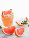 Cold lemonade of fresh grapefruit juice wihtout alcohole and ice cubes decorated a slice of grapefruit, twig mint and rosemary on