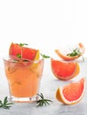 Cold lemonade of fresh grapefruit juice wihtout alcohole and ice cubes decorated a slice of grapefruit, twig mint and rosemary on