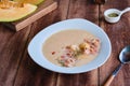 Cold melon soup with thin ham and fresh melon balls in a white ceramic plate on a brown wooden background. Spanish cuisine