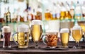 Cold mugs and glasses of beer on the old wooden table. Pub interior and bar counter with beer taps at the background. Assortment Royalty Free Stock Photo