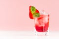 Cold red alcoholic liquor with ice cubes, strawberry slice, green mint in shot glass on white wood table and pastel pink wall. Royalty Free Stock Photo