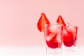 Cold red alcoholic liquors with ice cubes, strawberry slice in two shot glasses on white wood table and pastel pink wall. Royalty Free Stock Photo