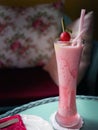 Cold red fruit juice in a tall glass decorated with 2 straws and cherry on a blue table, selective focus with dark background, Royalty Free Stock Photo