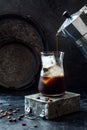 Cold refreshing iced coffee in a tall glass and coffee beans on dark background. Pouring coffee from moka pot into glass with ice Royalty Free Stock Photo