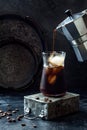 Cold refreshing iced coffee in a tall glass and coffee beans on dark background. Pouring coffee from moka pot into glass with ice Royalty Free Stock Photo
