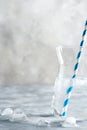 Cold refreshing natural water in a glass jar with plastic straw with ice cubes on a marble grey background.