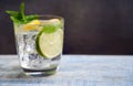 Cold refreshing summer limonade, mojito or gin tonic in glass, with fresh mint and ice cubes, lime and lemon on wooden table, on Royalty Free Stock Photo