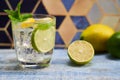 Cold refreshing summer limonade, mojito or gin tonic in glass, with fresh mint and ice cubes, lime and lemon on wooden table, on Royalty Free Stock Photo