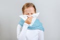 Cold season. Little girl in a warm scarf blows her nose. A child on a gray background