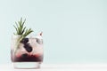 Cold shot in glass with blueberry, ice cubes, rosemary, straw in trendy modern bar interior in pastel mint color on white wood.