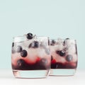 Cold shots in two glasses with blueberry, ice cubes in trendy modern bar interior in pastel mint color on white wood board, square