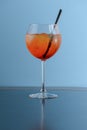 Cold summer alcohol cocktail with ice and orange in a wine glass and black plastic straw on light pastel blue background Royalty Free Stock Photo