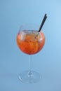 Cold summer alcohol cocktail with ice and orange in a wine glass and black plastic straw on light pastel blue background Royalty Free Stock Photo