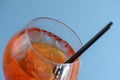 Cold summer alcohol cocktail with ice and orange in a wine glass and black plastic straw on light pastel blue background Royalty Free Stock Photo