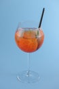 Cold summer alcohol cocktail with ice and orange in a wine glass and black plastic straw on light pastel blue background Royalty Free Stock Photo