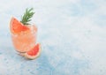 Cold summer grapefruit cocktail in glass with ice cubes and rosemary with grapefruits slice on blue background