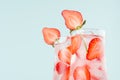 Cold summer strawberry water with strawberry slices, ice cubes, soda in misted glass on pastel green color background, closeup.