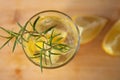 Cold vitamin drink with lemon and sprig of rosemary on a wooden background